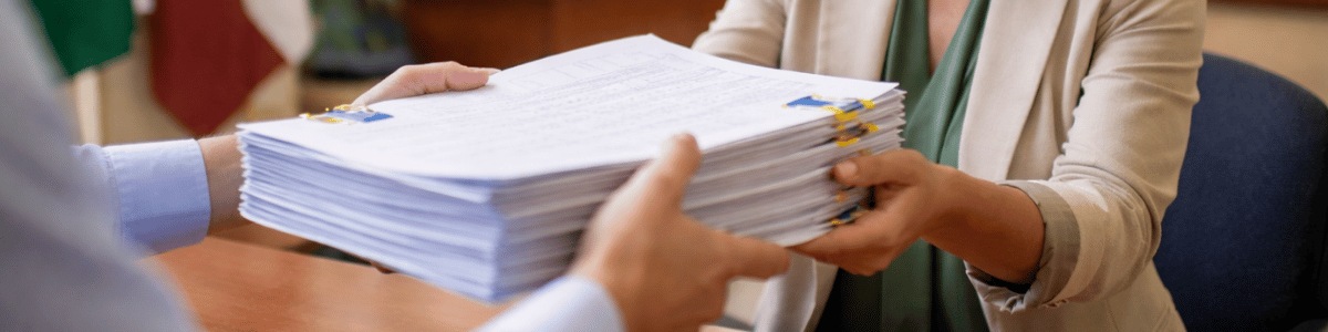 documentos para nomeação em cargo público Pessoa entrega uma pilha organizada de documentos a uma servidora em ambiente interno de prefeitura, com clima institucional e iluminação natural suave
