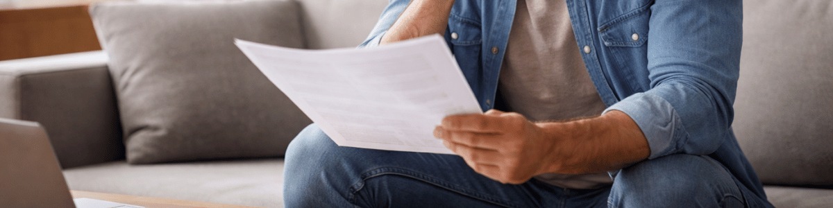 certidão de indisponibilidade de bens Pessoa sentada em um sofá de casa, observando atentamente um documento em um ambiente interno bem iluminado, com luz natural suave, transmitindo concentração e reflexão em um contexto doméstico e informativo