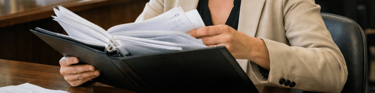 como descobrir se a pessoa é casada Mulher sentada em um ambiente de cartório, analisando atentamente vários documentos organizados em uma pasta, com expressão concentrada