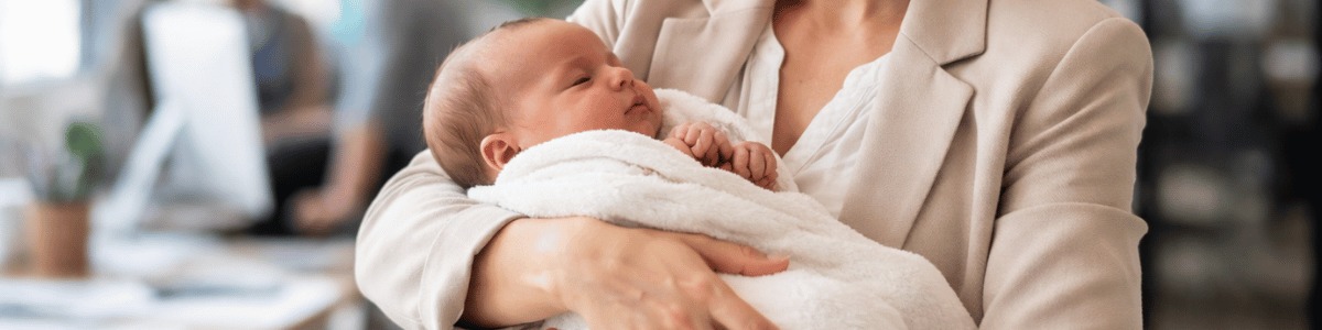 Uma mãe segura com delicadeza seu recém-nascido no colo em um ambiente de trabalho moderno, iluminado por luz natural, transmitindo cuidado, acolhimento e a conciliação entre maternidade e vida profissional