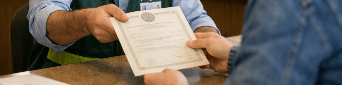 certidão negativa de tributos mobiliários A imagem mostra um funcionário da prefeitura entregando uma certidão a um cidadão em um balcão de atendimento. O ambiente é institucional, bem iluminado e organizado, com outros atendentes ao fundo. A cena transmite um momento formal de atendimento, com foco na interação e na entrega do documento.