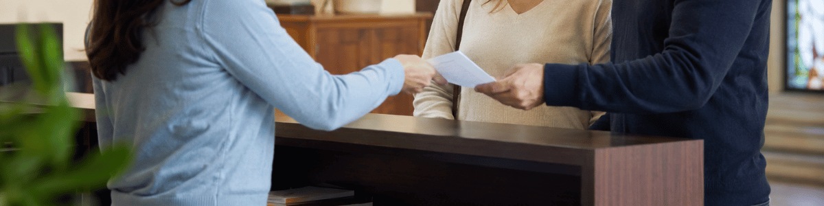 Casal recebe um documento no balcão de uma paróquia, em um ambiente acolhedor e institucional, com iluminação suave e detalhes religiosos discretos ao fundo.
