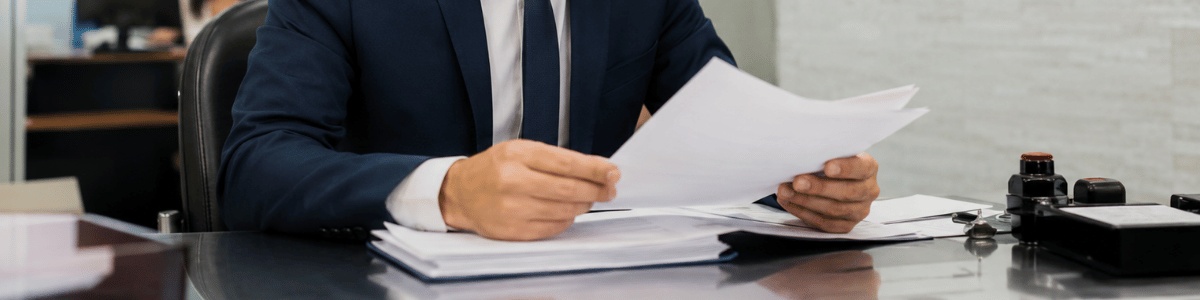 prazo proclamas de casamento Profissional de cartório analisando documentos de proclamas de casamento em uma mesa de atendimento, com expressão concentrada e ambiente institucional ao fundo. A cena transmite seriedade, organização e atenção aos detalhes do processo matrimonial.