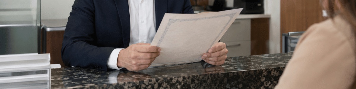 Funcionário de cartório analisa atentamente uma certidão no balcão de atendimento, em um ambiente moderno e profissional, enquanto uma cliente aguarda à frente.