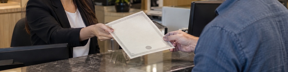 Pessoa recebendo uma certidão das mãos de uma atendente em um cartório, em ambiente profissional, organizado e com iluminação suave