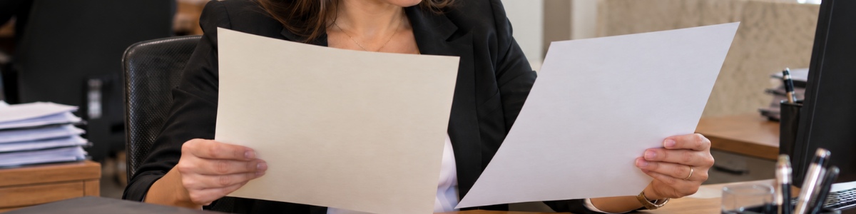 Funcionária de cartório comparando duas certidões sobre a mesa, em um ambiente profissional e organizado, com expressão atenta e iluminação suave